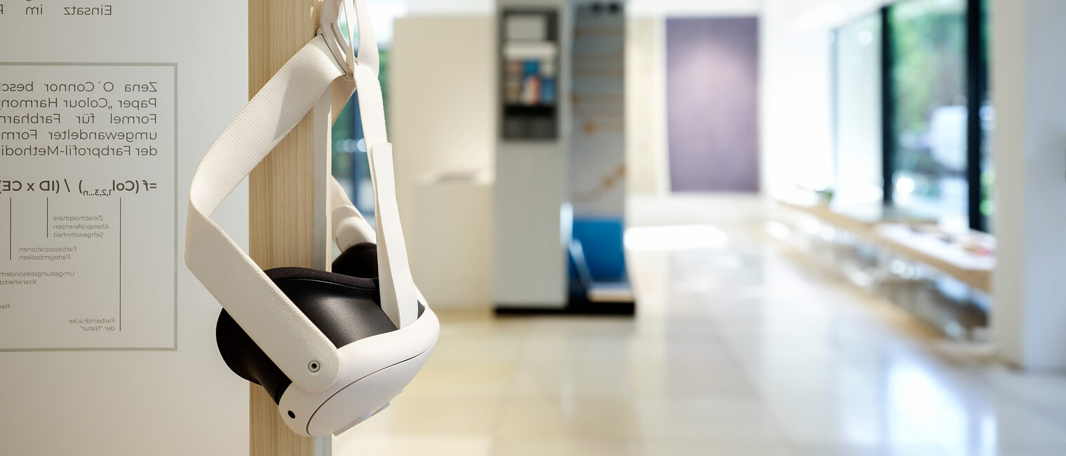 Impression der Ausstellung Farbe im Raum. Unscharfer Blick in den Galerieraum. Im Vordergrund hängt eine VR-Brille am Haken.