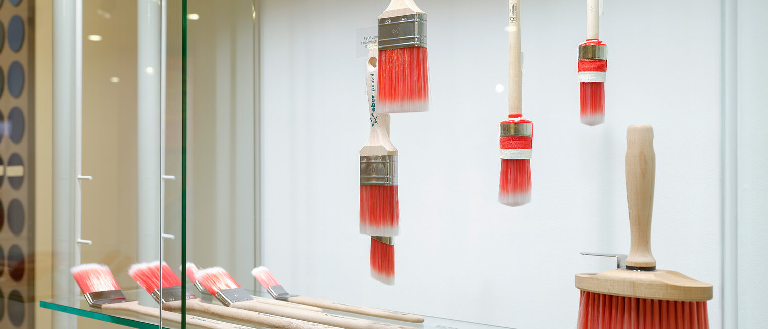 Verschiedene Größen an handgefertigten Maler-Pinseln mit orange-weißen Borsten in einer Vitrine