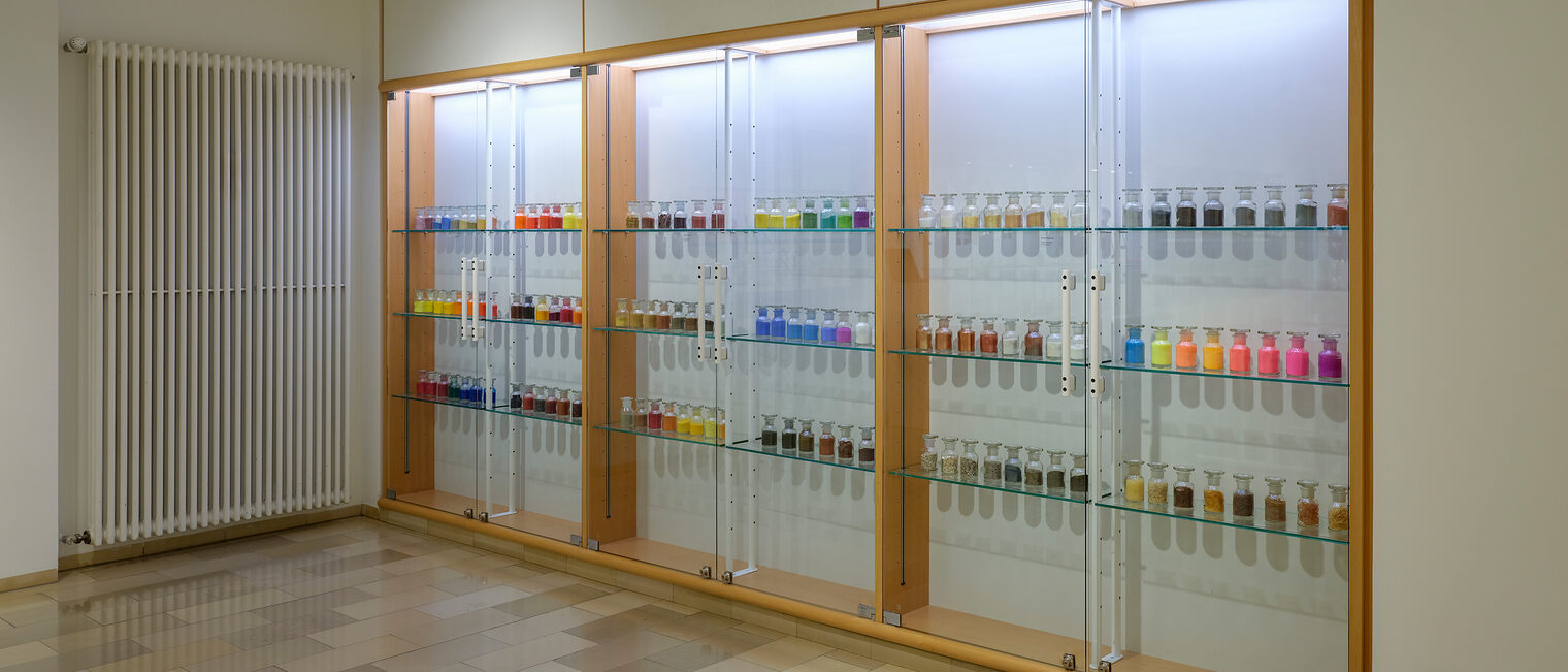 Drei große beleuchtete Vitrinen gefüllt mit bunten Fläschchen mit Farbpigmenten in der Ausstellung Farbe im Raum.