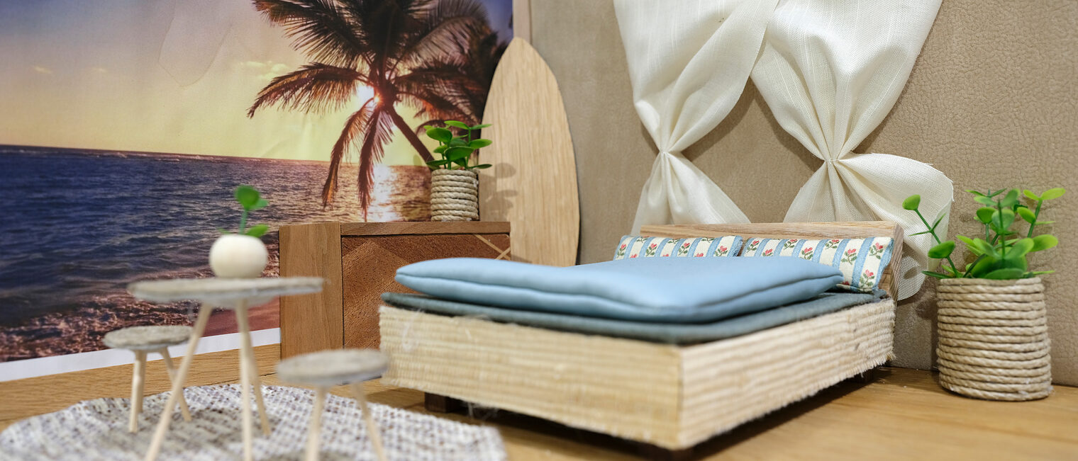 Kleines 3-D-Modell eines Schlafzimmers mit Strand-Fototapete, Doppelbett, weißen Vorhängen, Tisch mit 2 Hockern, Surfbrett.