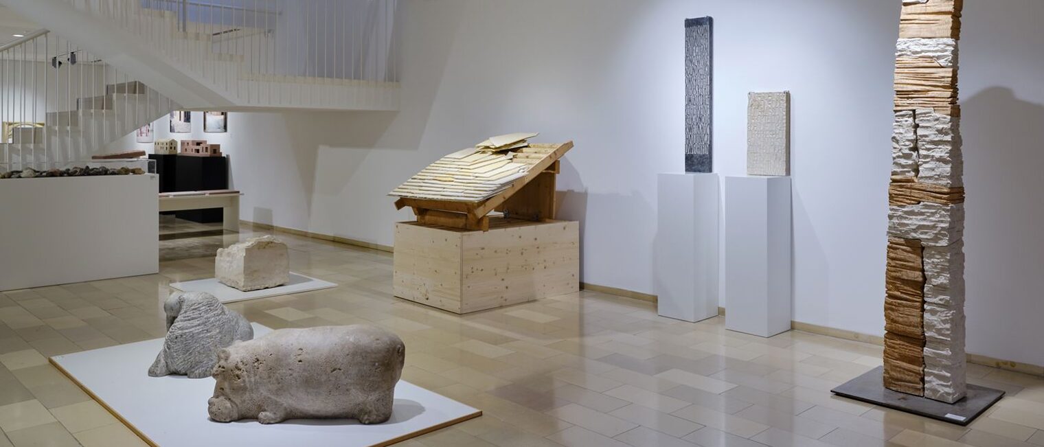 Auf dem Boden zwei Steinkissen, daneben eine etwa 2 Meter große Stele aus Ziegelsteinen