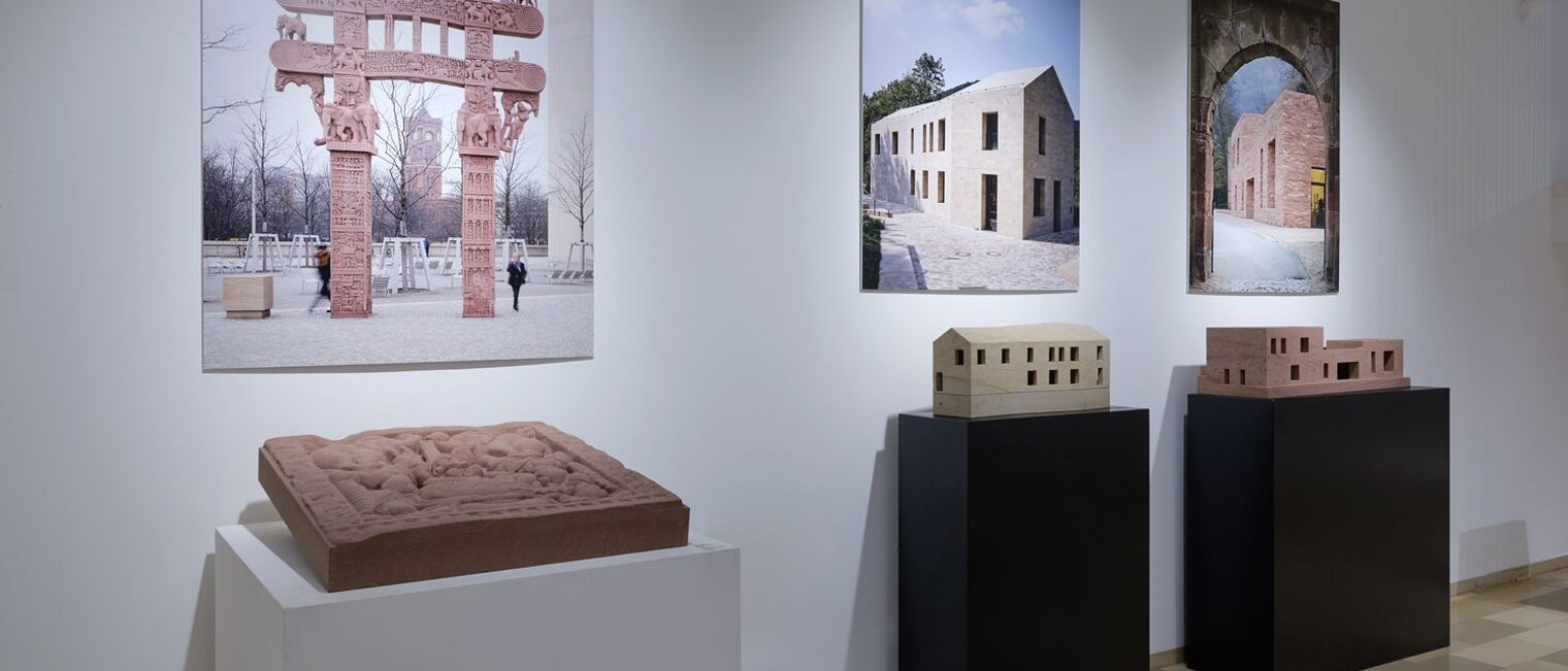 braune Steintafel liegend auf einer Säule platziert, darüber ein Foto eines buddhistischen Toreingangs in derselben Farbe.