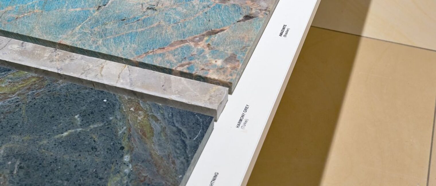 Entlang dem Treppengelaende liegen farbige Marmorplatten mit lebhaften Einschluessen von tuerkis ueber hellblau bis braun.