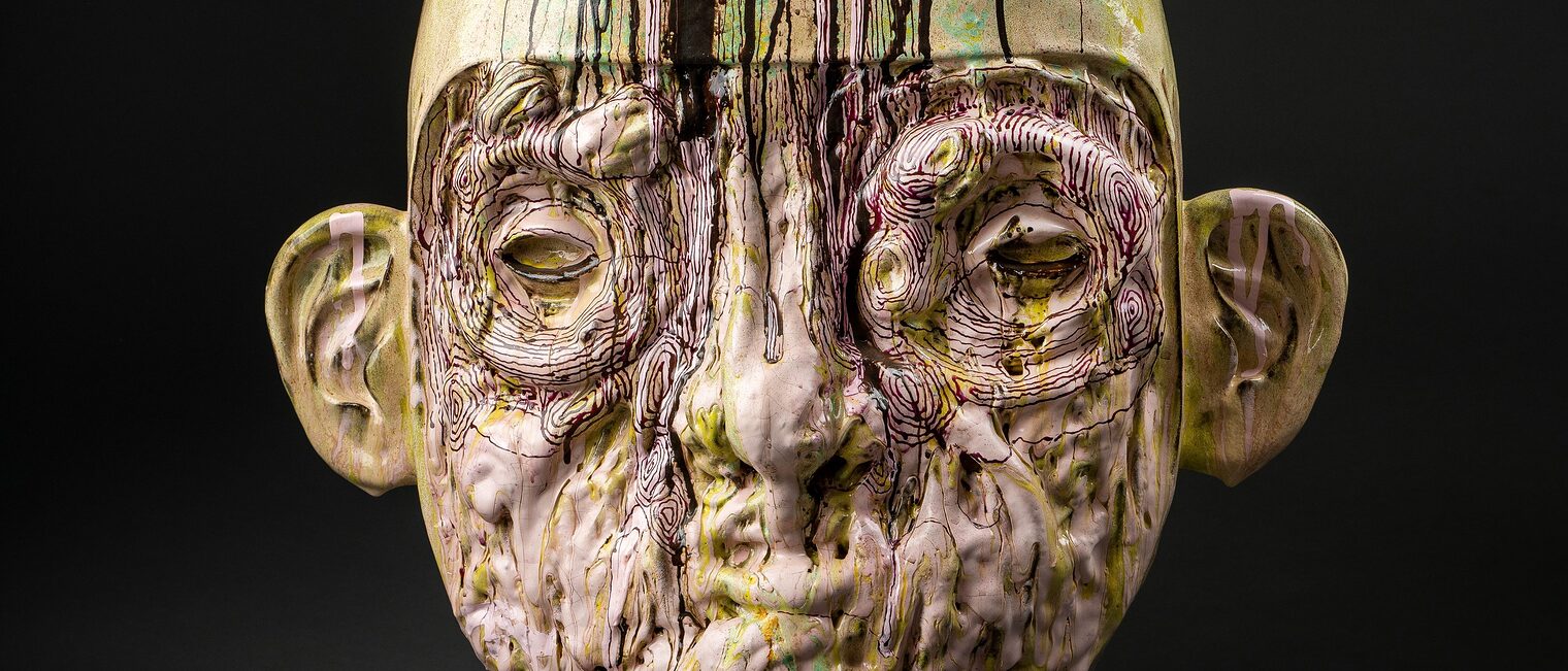 Hautfarbener, mit hellgrünen Schlieren durchzogener Männerkopf mit filigranem braunem Linienmuster aus Keramik