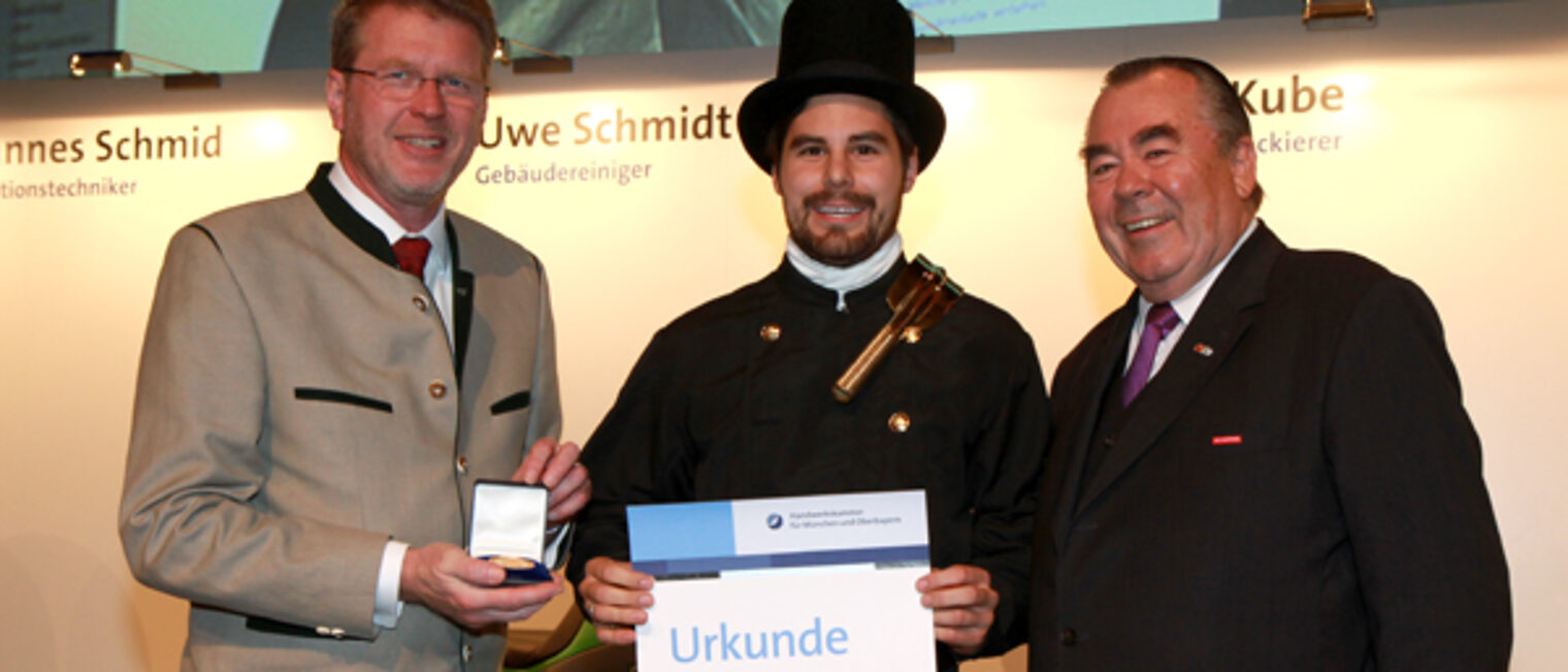 Handwerkskammerpräsident Heinrich Traublinger, MdL a. D. (rechts) und Umweltminister Dr. Marcel Huber, MdL (links) überreichten Kaminkehrermeister Jürgen Schwaiger seine Urkunde als Jahresbestmeister.